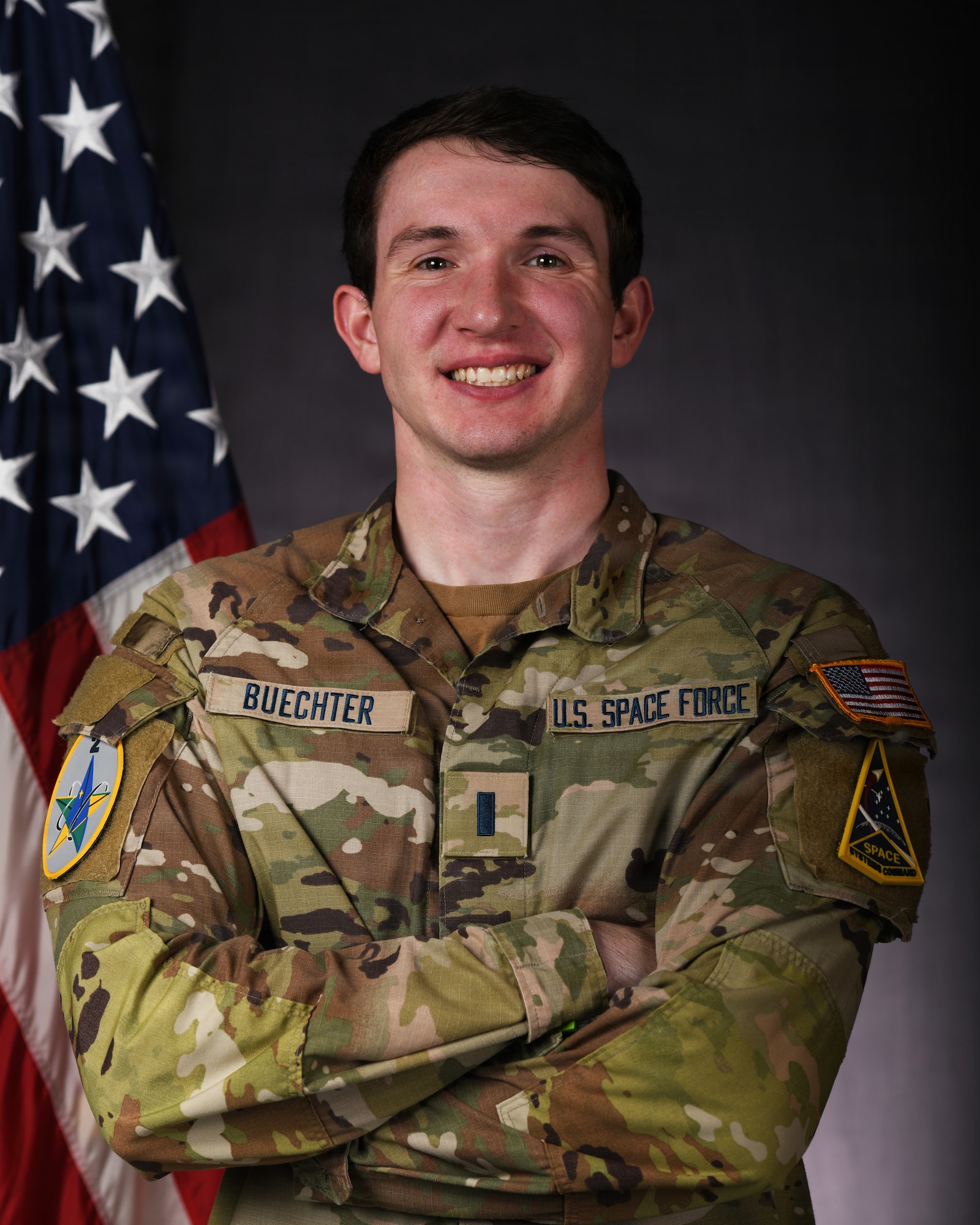 a person in military uniform poses next to a us flag and smiles for a photo