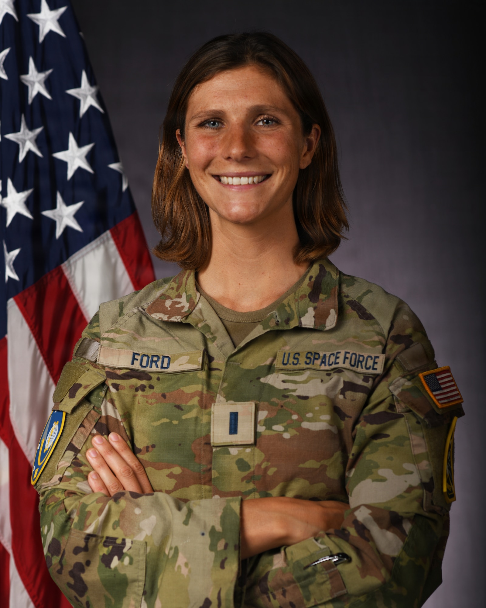 a person in military uniform poses next to a us flag and smiles for a photo
