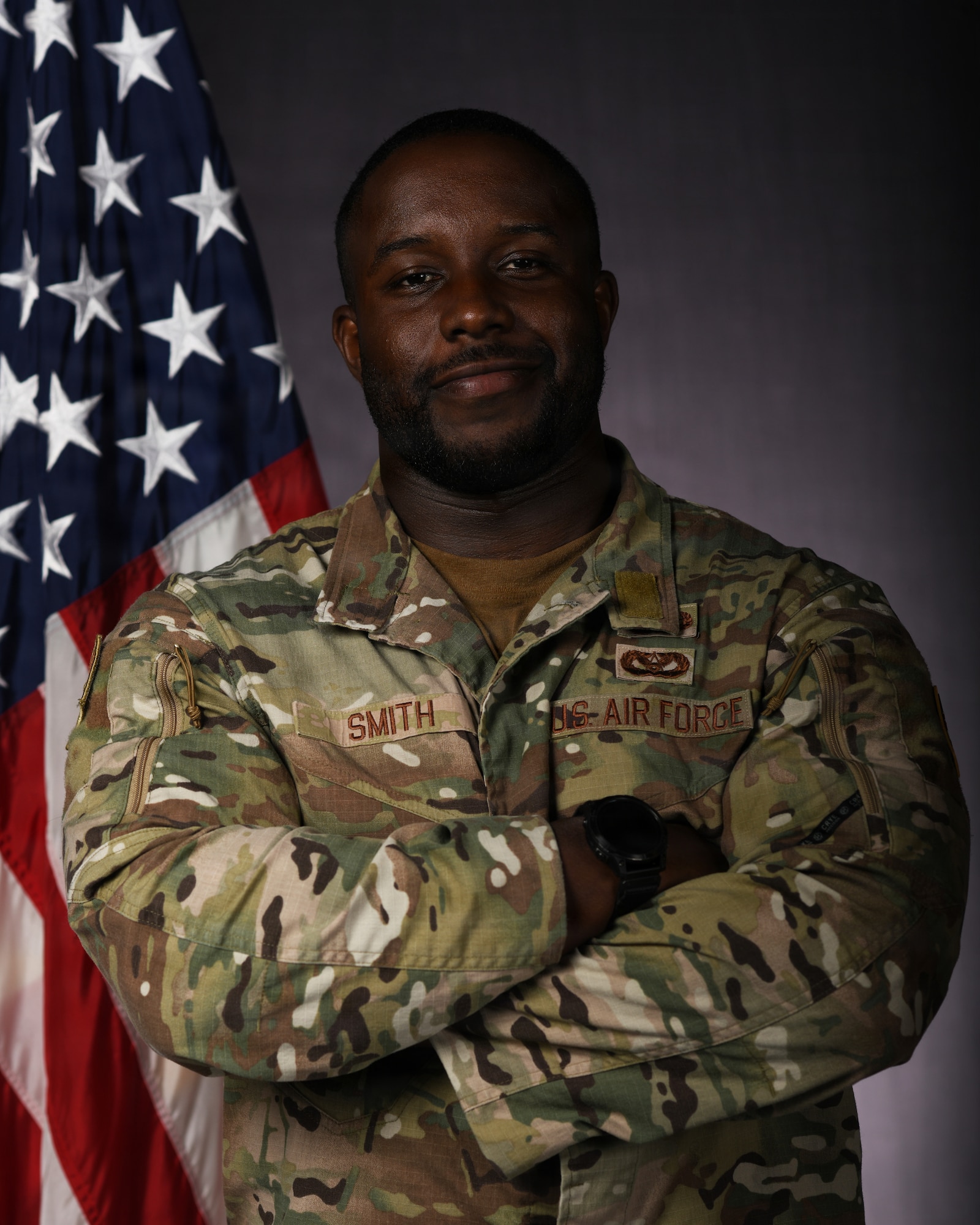 a person in military uniform poses next to a us flag and smiles for a photo