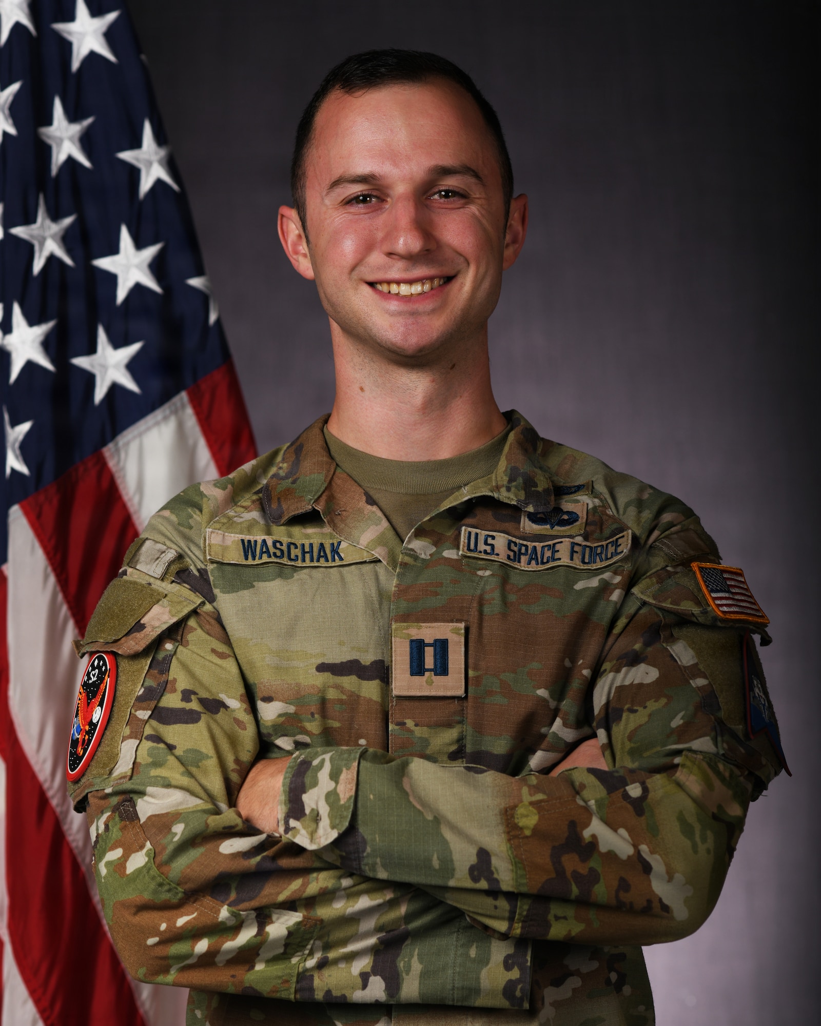 a person in military uniform poses next to a us flag and smiles for a photo