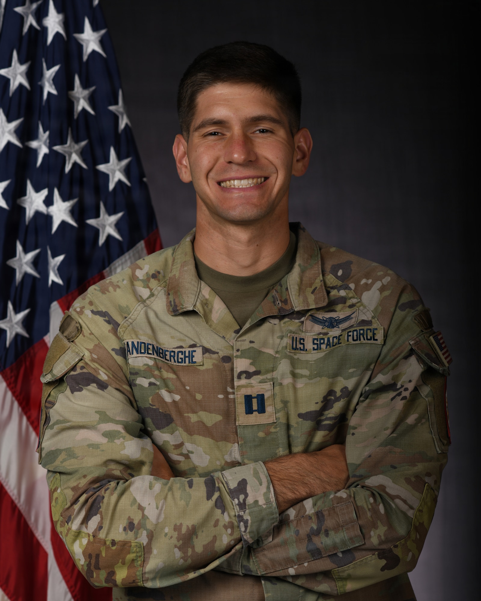 a person in military uniform poses next to a us flag and smiles for a photo