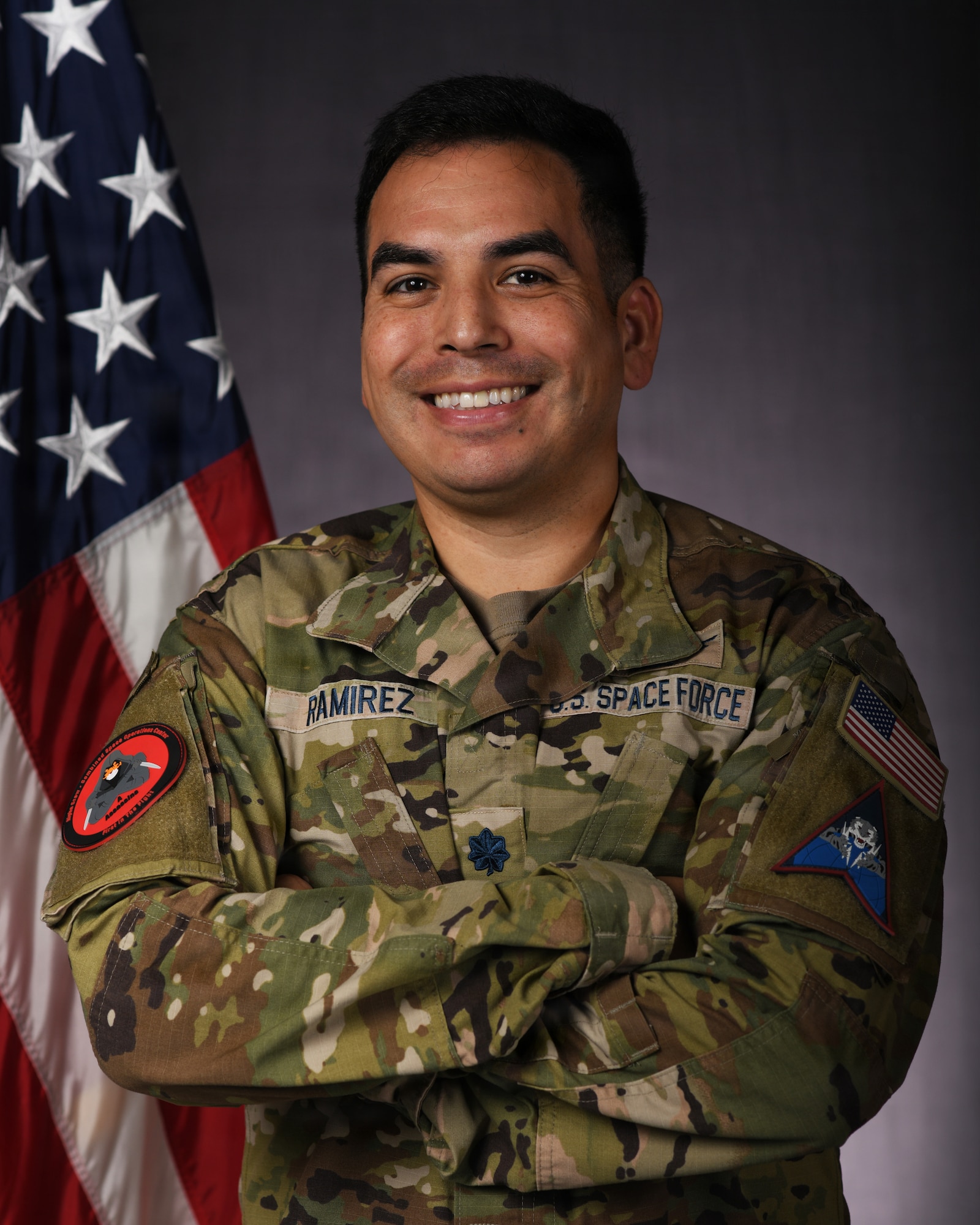 a person in military uniform poses next to a us flag and smiles for a photo