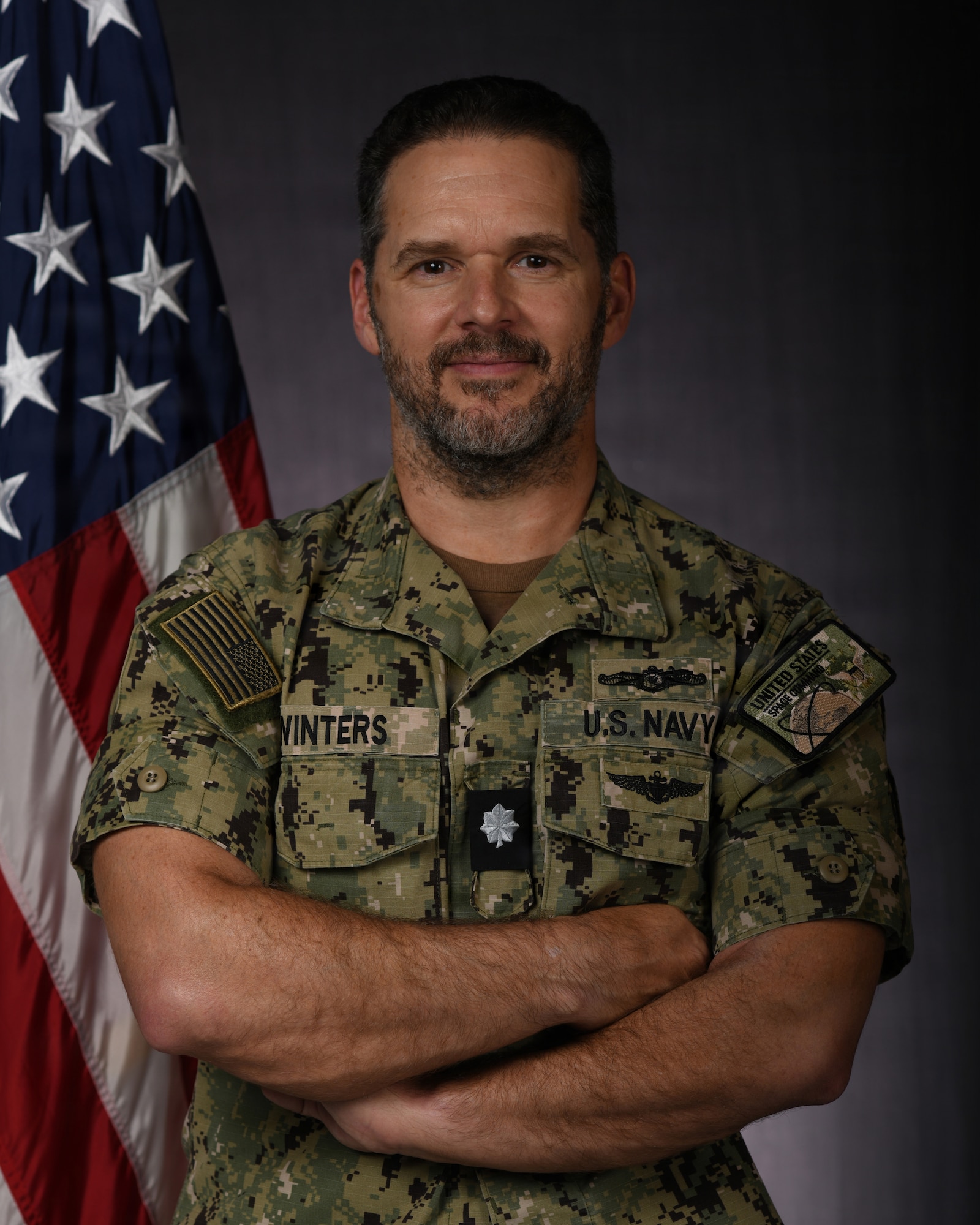 a person in military uniform poses next to a us flag and smiles for a photo