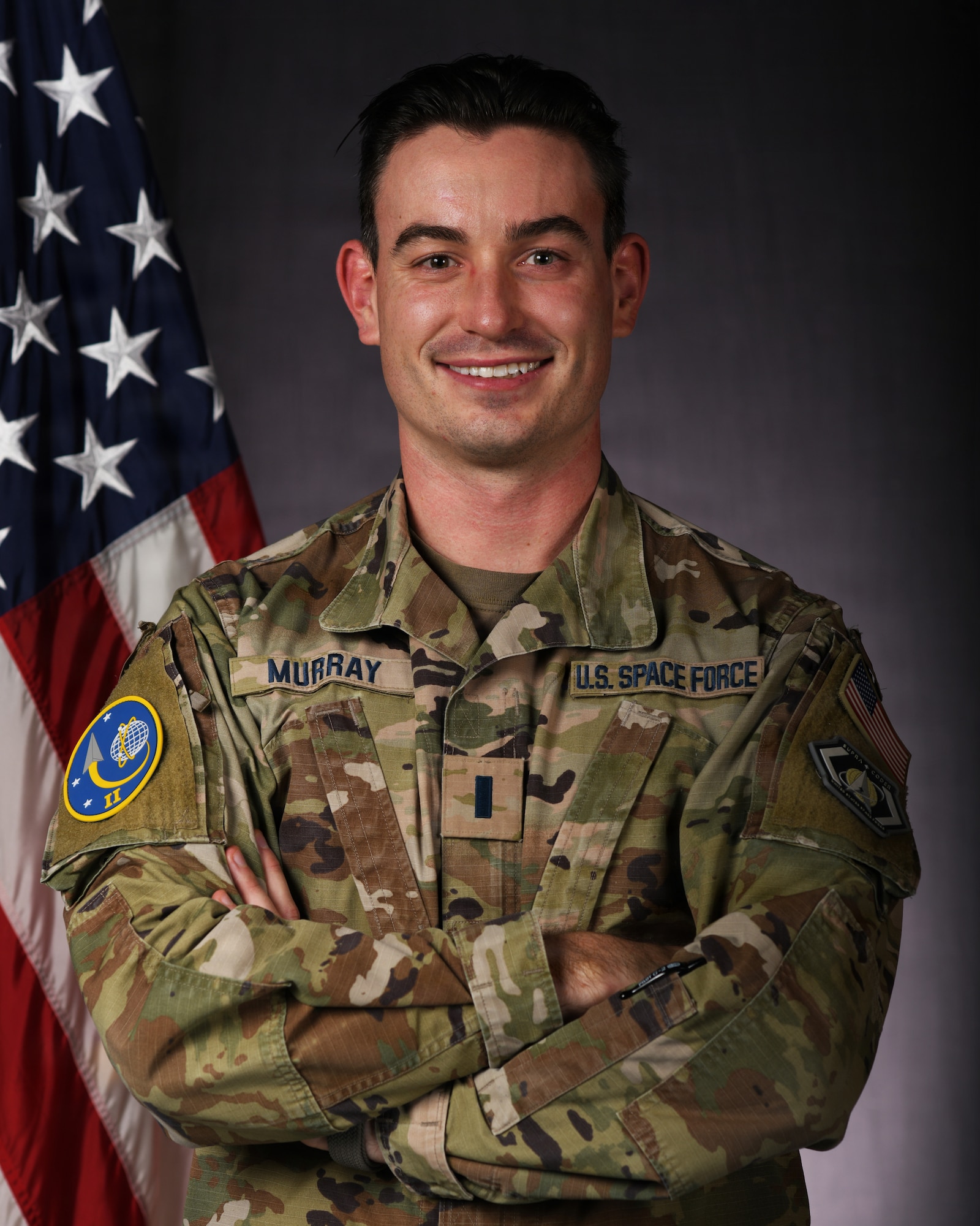 a person in military uniform poses next to a us flag and smiles for a photo