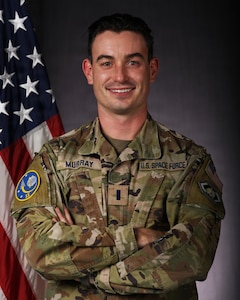 a person in military uniform poses next to a us flag and smiles for a photo