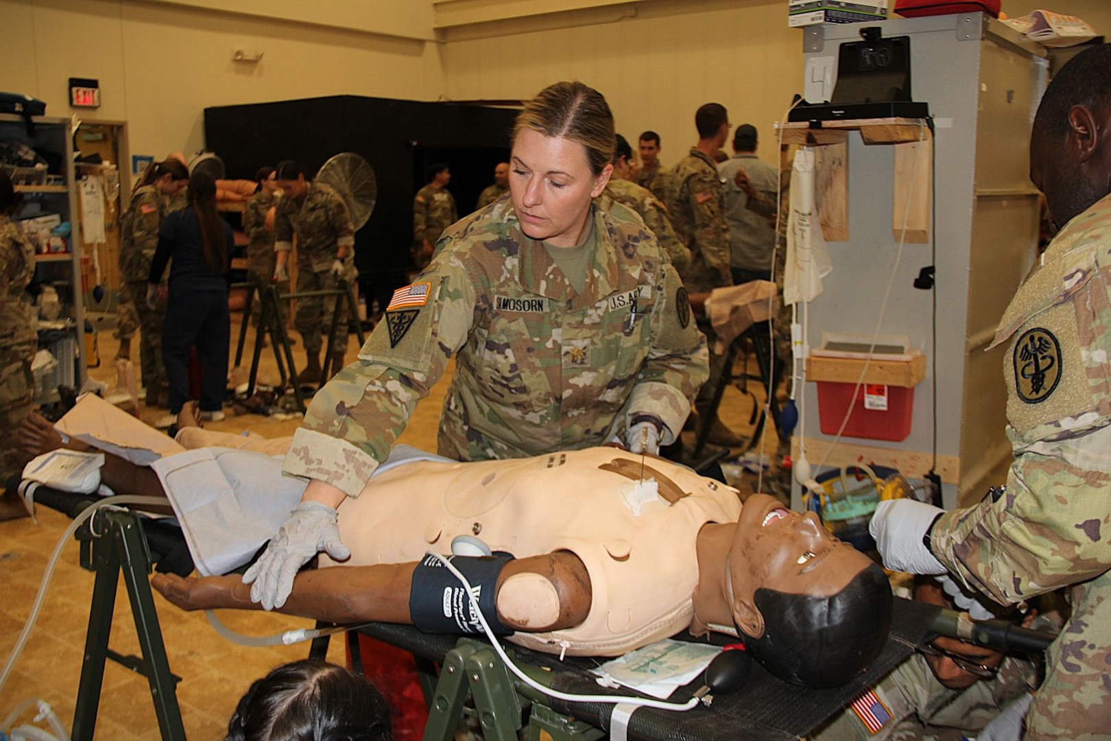 Uniformed service member stands over simulated patient.