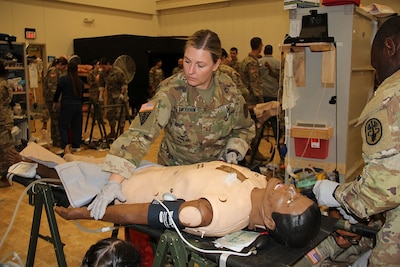 Uniformed service member stands over simulated patient.