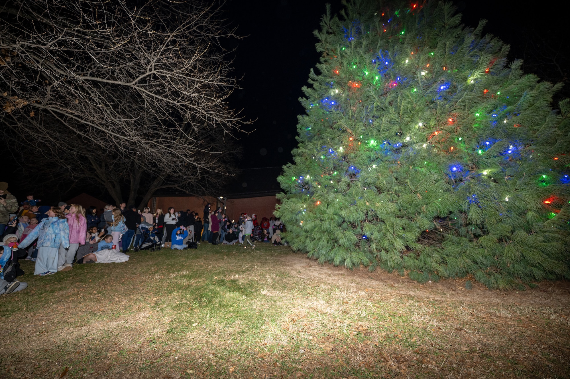 Team Dover families gather around a newly lit Christmas tree at the conclusion of the annual holiday parade at Dover Air Force Base, Delaware, Dec. 1, 2025. The parade and tree lighting are traditions marking the start of the holiday season for Dover AFB. (U.S. Air Force photo by Mauricio Campino)