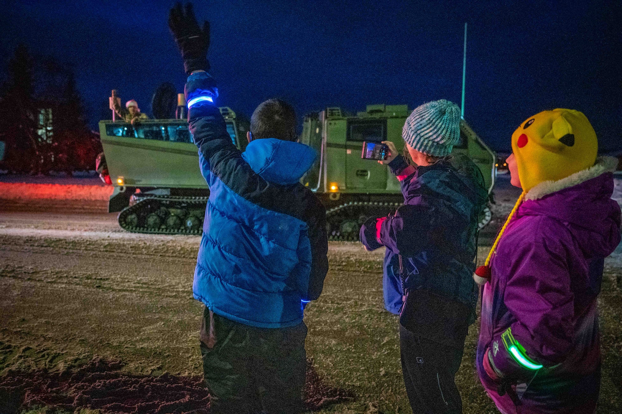 Children wave as base leadership passes by in a U.S. Army Cold-Weather All-Terrain Vehicle (CATV) during the annual Tree Lighting Ceremony at Joint Base Elmendorf-Richardson, Alaska, Nov. 25, 2025. The 773d Force Support Squadron hosts the ceremony annually to promote community readiness and cohesion during the holiday season. (U.S. Air Force photo by Senior Airman Hunter Hites)