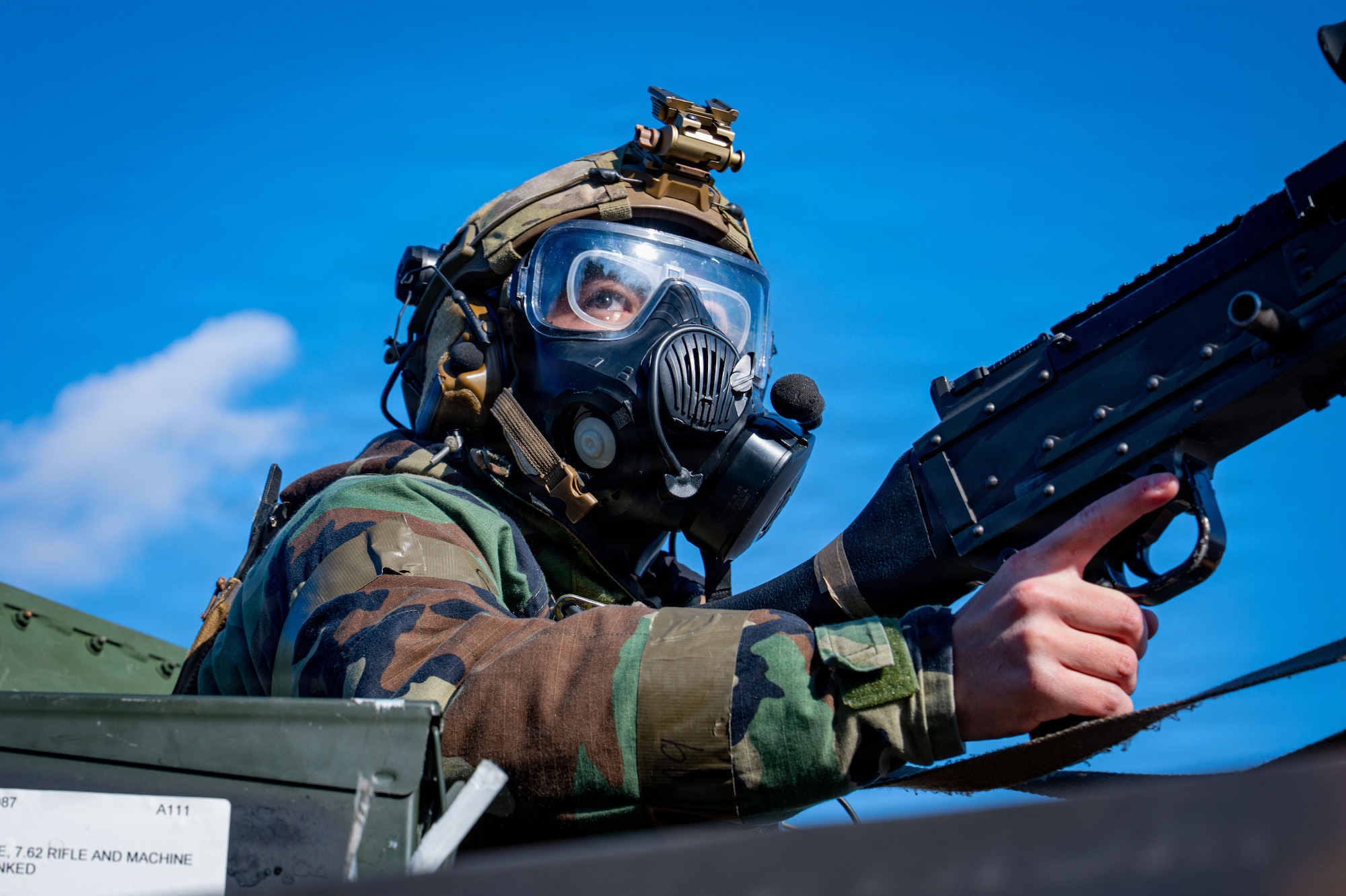 A cop in a gas mask looks right while indexing a machine gun