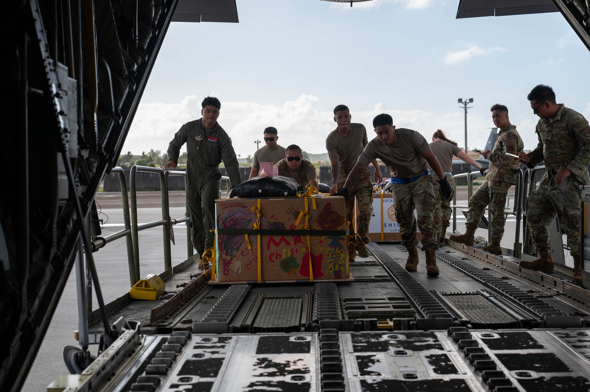 Military members push a box onto a C-130J aircraft.