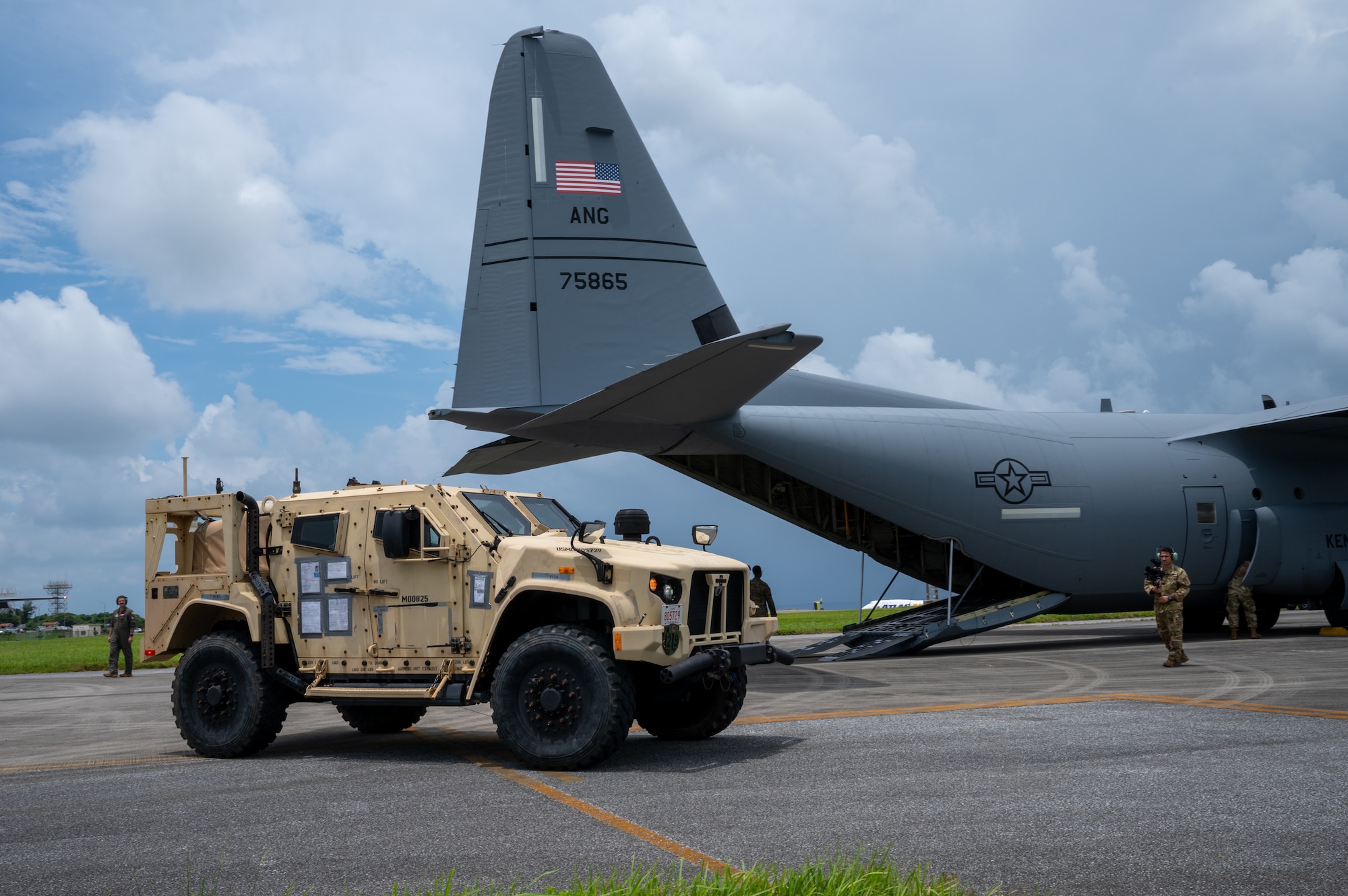 A tactical vehicle parks in front of an aircraft before boarding on a flight line