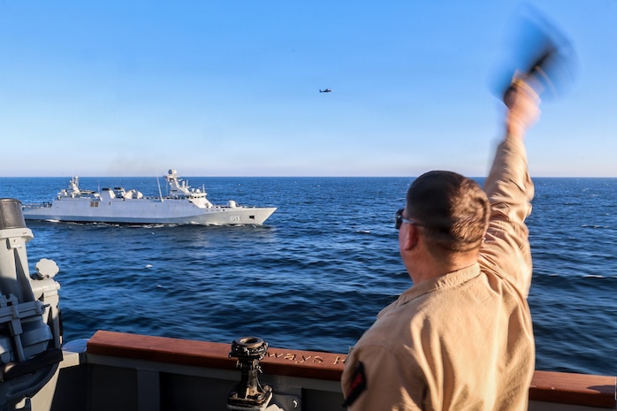 Cmdr. Joseph Phillips, commanding officer of the Arleigh-Burke-class guided-missile destroyer USS Paul Ignatius (DDG 117), waves to The Royal Moroccan Navy frigate Tarik Ben Ziyad (FSG 613) during a passing exercise as the Moroccan HH-65A Dolphin helicopter collects photos, Dec. 2, 2025.