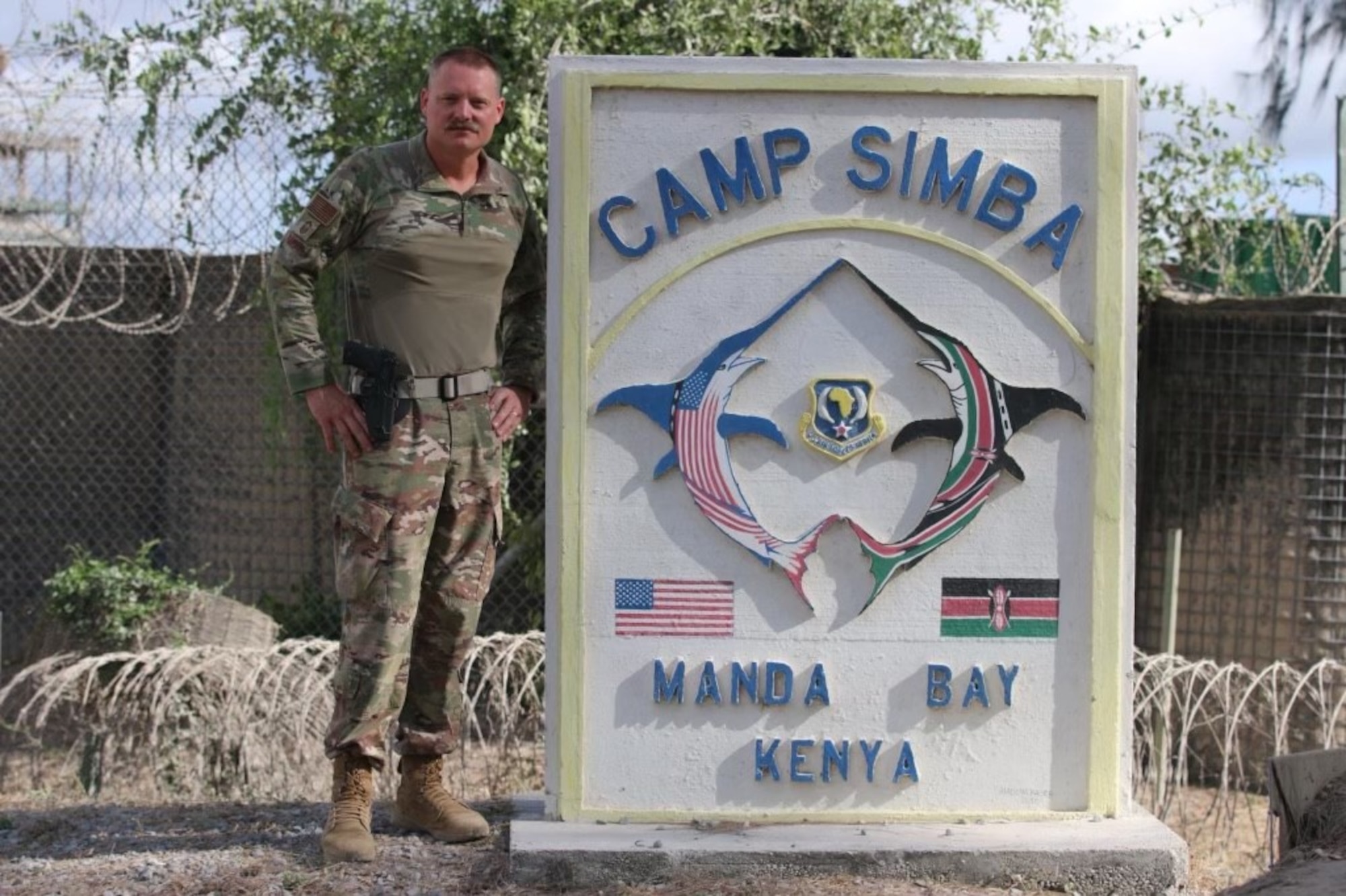 U.S. Air Force Chief Master Sgt. Frank Rawls stands in front of the Camp Simba sign for a photo while being deployed to Operation OCTAVE SHIELD at Manda Bay, Kenya, March 22, 2022.