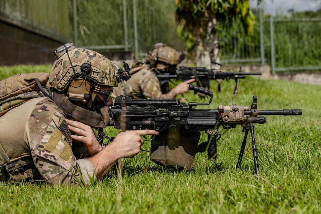 Navy SEALs lie on the grass in formation while aiming weapons.