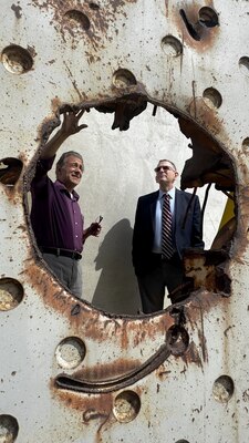 Two men are seen through a blast hole of a piece of steel