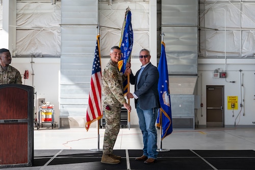 U.S. Air Force Col. Jose Cabrera, 355th Wing commander, presents a guidon to Benjamin Fernandez, DM50 president, inducting him as 355th Wing honorary commander at Davis-Monthan Air Force Base, Arizona, Dec. 8, 2025. Fernandez, a Tucson native, is the president of DM50, an organization dedicated to enhancing the quality of life for Airmen at DM. (U.S. Air Force photo by Airman 1st Class Samantha Melecio)