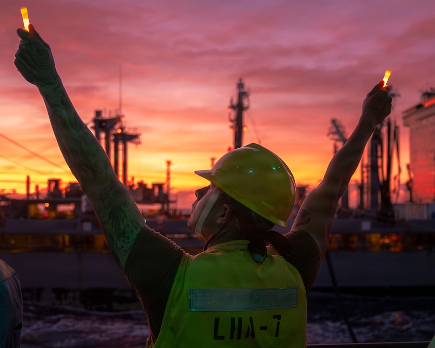 Boatswain’s Mate 2nd Class Ruben Zavala, assigned to the America-class amphibious assault ship USS Tripoli (LHA 7) signals to the Kaiser-class underway replenishment oiler USNS Tippecanoe (T-AO 199) during a replenishment-at-sea in the South China Sea, Dec. 6, 2025.