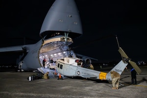The front of a C-5M Super Galaxy aircraft is opened for the loading of a UH-1N Huey helicopter.