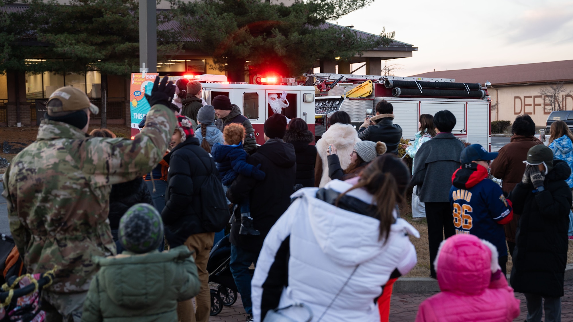U.S. Airmen and family members from the Osan community wave at Santa Claus as he rides by in a 51st Civil Engineer Squadron fire truck during the Christmas Tree Lighting Ceremony at Osan Air Base, Republic of Korea, Dec. 5, 2025. The gathering provided Airmen and families an opportunity to reconnect, celebrate and support one another during the holiday season. (U.S. Air Force photo by Senior Airman Rome Bowermaster)