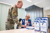 Master Sgt. Anthony Eberly, 59th Medical Wing volunteer services coordinator, reviews information desk procedures with volunteer Sharon Disler at the Wilford Hall Ambulatory Surgical Center, Joint Base San Antonio–Lackland, Texas, Dec. 4, 2025.