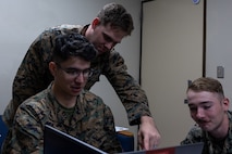 U.S. Marine Corps Sgt. Michael Saris II, top left, a native of Pennsylvania, and Cpl. Alex Hunt, right, a native of Maryland, instruct Lance Cpl. Christopher Camareno, a native of Florida, all cyberspace warfare operators with 3d Cyber Warfare Company, III Marine Expeditionary Force Information Group, during the Marine Corps Cyber Red Zone 26-1 event at Camp Courtney, Okinawa, Japan, Nov. 4, 2025. Cyber Red Zone challenged Marines to find and defend networks against simulated cyberattacks, improving the Marine Corps’ ability to fight and win in the information domain. (U.S. Marine Corps photo by Lance Cpl. John-Paul Haubeil)