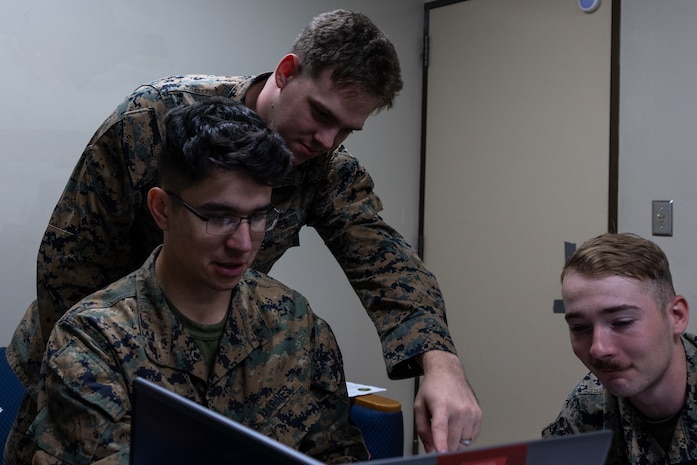 U.S. Marine Corps Sgt. Michael Saris II, top left, a native of Pennsylvania, and Cpl. Alex Hunt, right, a native of Maryland, instruct Lance Cpl. Christopher Camareno, a native of Florida, all cyberspace warfare operators with 3d Cyber Warfare Company, III Marine Expeditionary Force Information Group, during the Marine Corps Cyber Red Zone 26-1 event at Camp Courtney, Okinawa, Japan, Nov. 4, 2025. Cyber Red Zone challenged Marines to find and defend networks against simulated cyberattacks, improving the Marine Corps’ ability to fight and win in the information domain. (U.S. Marine Corps photo by Lance Cpl. John-Paul Haubeil)