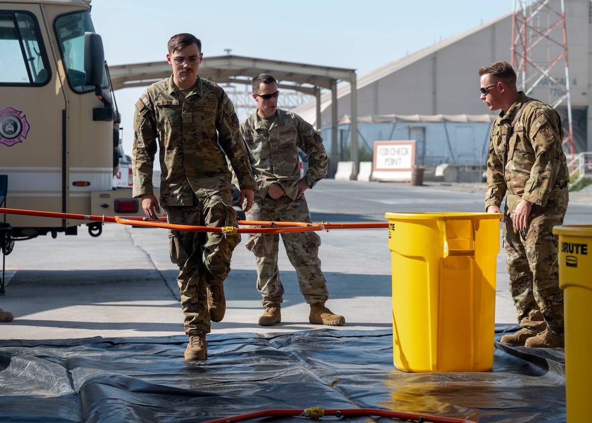 A man in a military uniform stands on one leg as other men in military uniforms raise a metal hooparound his body.