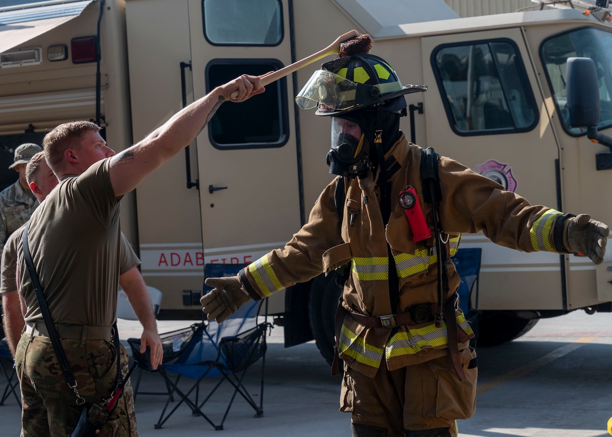 A man scrubs the helmet of a man in a firefighter unifrom.