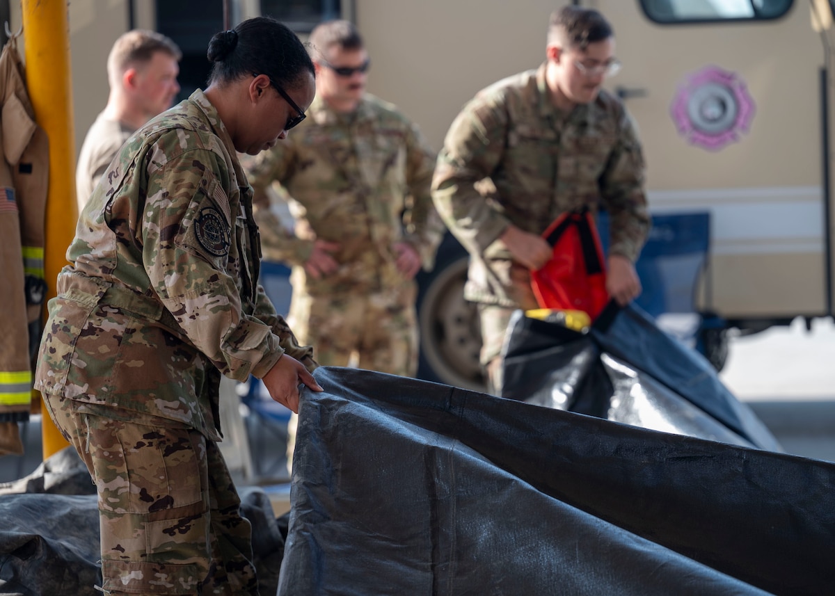 A woman in a military uniform hold the edge of a large black tarp.