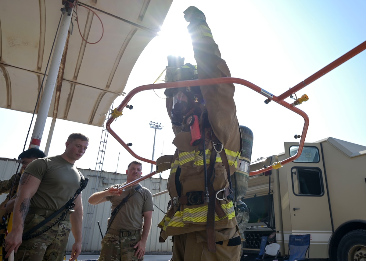 A man in a firefighter uniform raises his arms inside a metal hoop.
