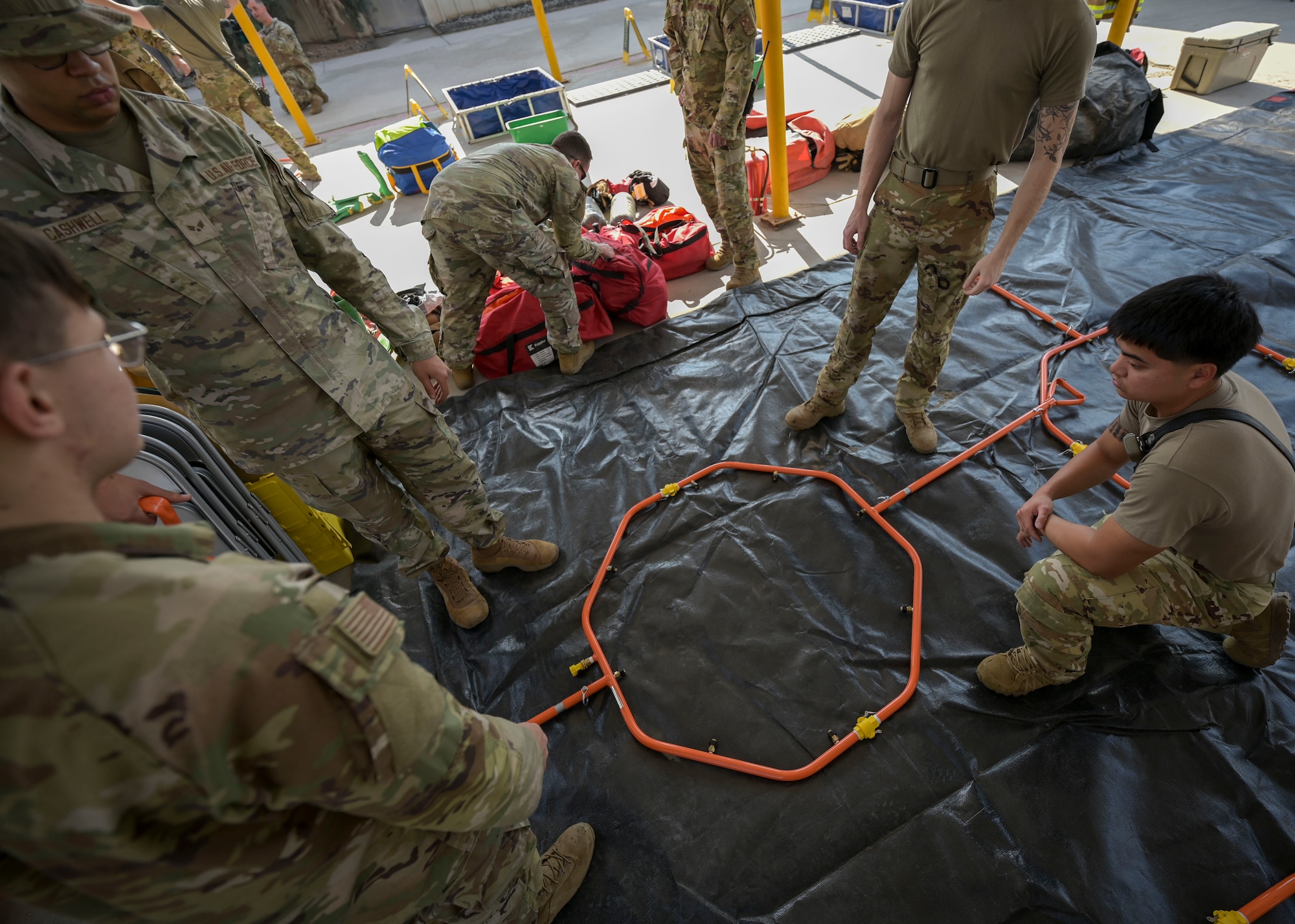Men in military uniforms assemble a ornage metal hoop.