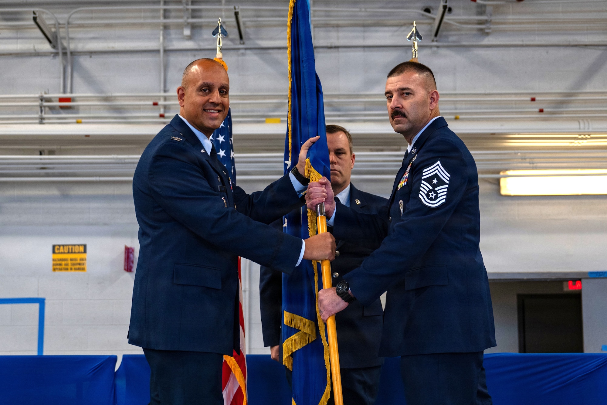 Photo of U.S. Air Force Col. Mansour Elhihi, 125th Fighter Wing commander (left), in dress blues, passing the 125th FW guidon to U.S. Air Force Chief Master Sgt. William Ryals, also in dress blues, who is the incoming 125th FW command Chief (right), during a change of responsibility ceremony at the 125th Fighter Wing in Jacksonville, Florida, Dec. 6, 2025.