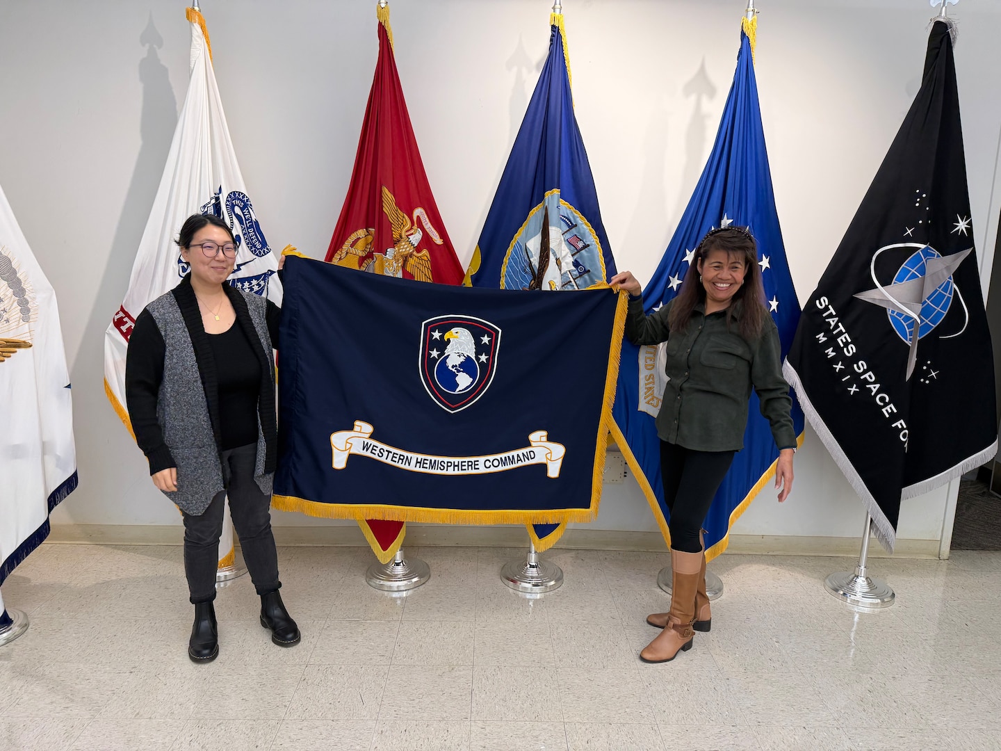 two women hold up a blue flag with an eagle, globe and written scroll, with gold fringe