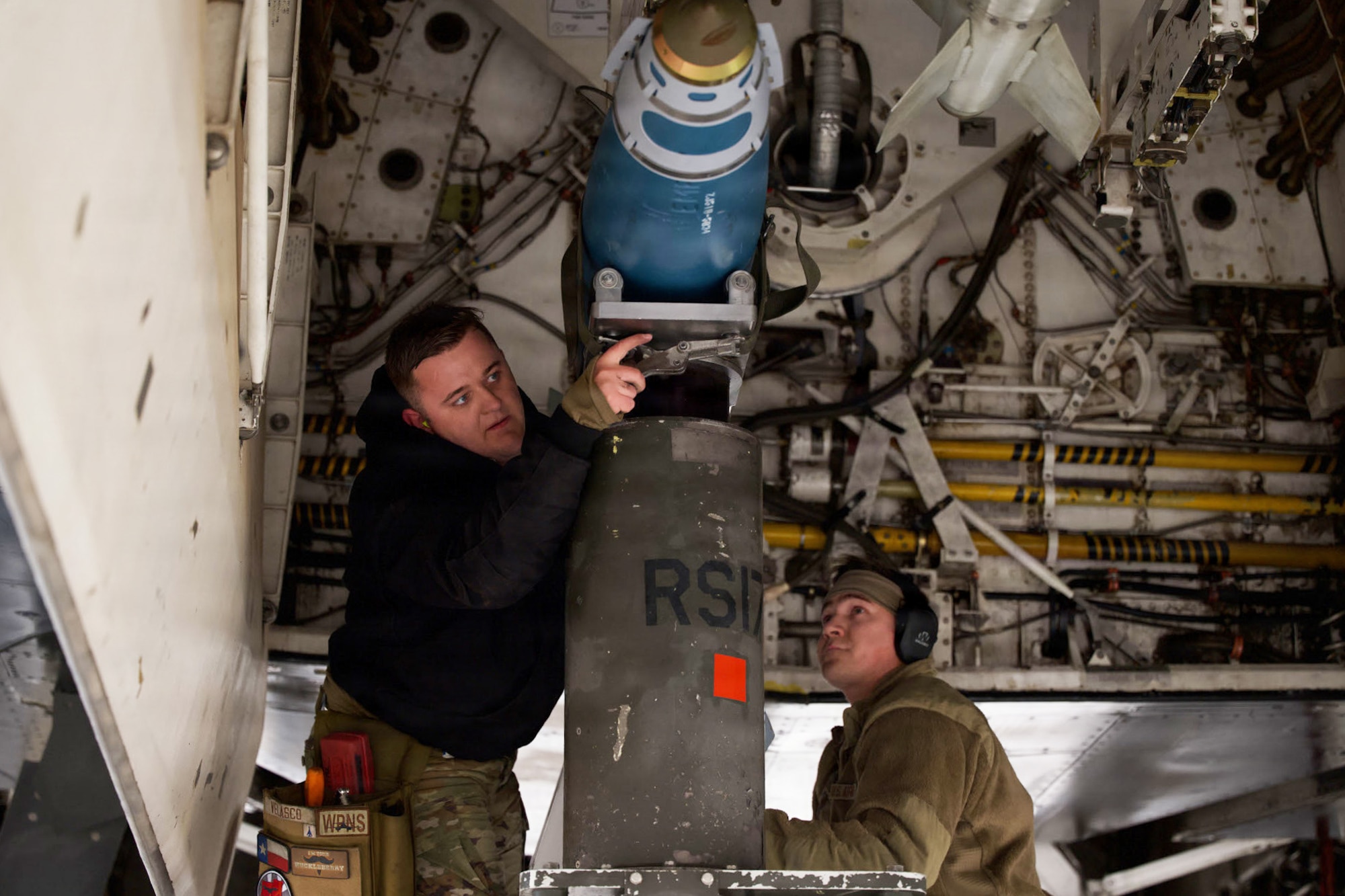 U.S. Air Force Staff Sgt. Jordan Arthur, 28th Bomber Generation Squadron weapons load crew chief, right, and Airman 1st Class Ryan Velasco, 9th BGS weapons load crew member, load a guided bomb unit onto a B-1B Lancer during the annual Weapons Load Crew of the Year competition at Dyess Air Force Base, Texas, Dec. 4, 2025. Teams were tasked with loading air-to-ground missiles and GBU-38s as part of the event. (U.S. Air Force photo by Senior Airman Emma Anderson)