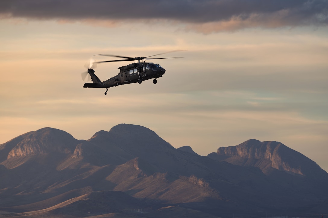 A black helicopter flies in a hazy sky over mountains.