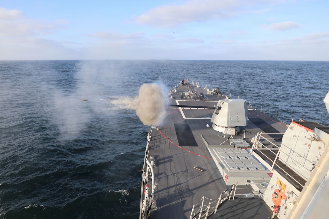 Ammo flies over a body of water after a ship fires a weapon, leaving behind clouds of smoke.