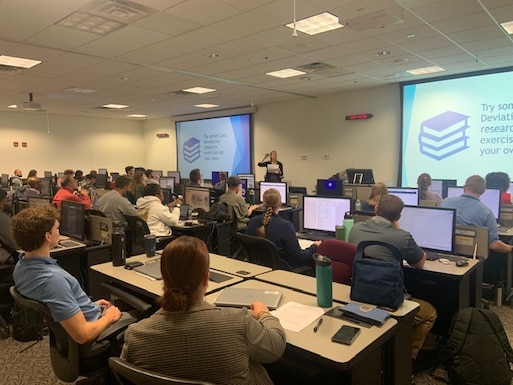 A classroom full of computer stations and students sitting at them.
