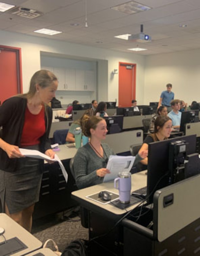 A room full of people sitting at computers. It is a classroom with students in it.
