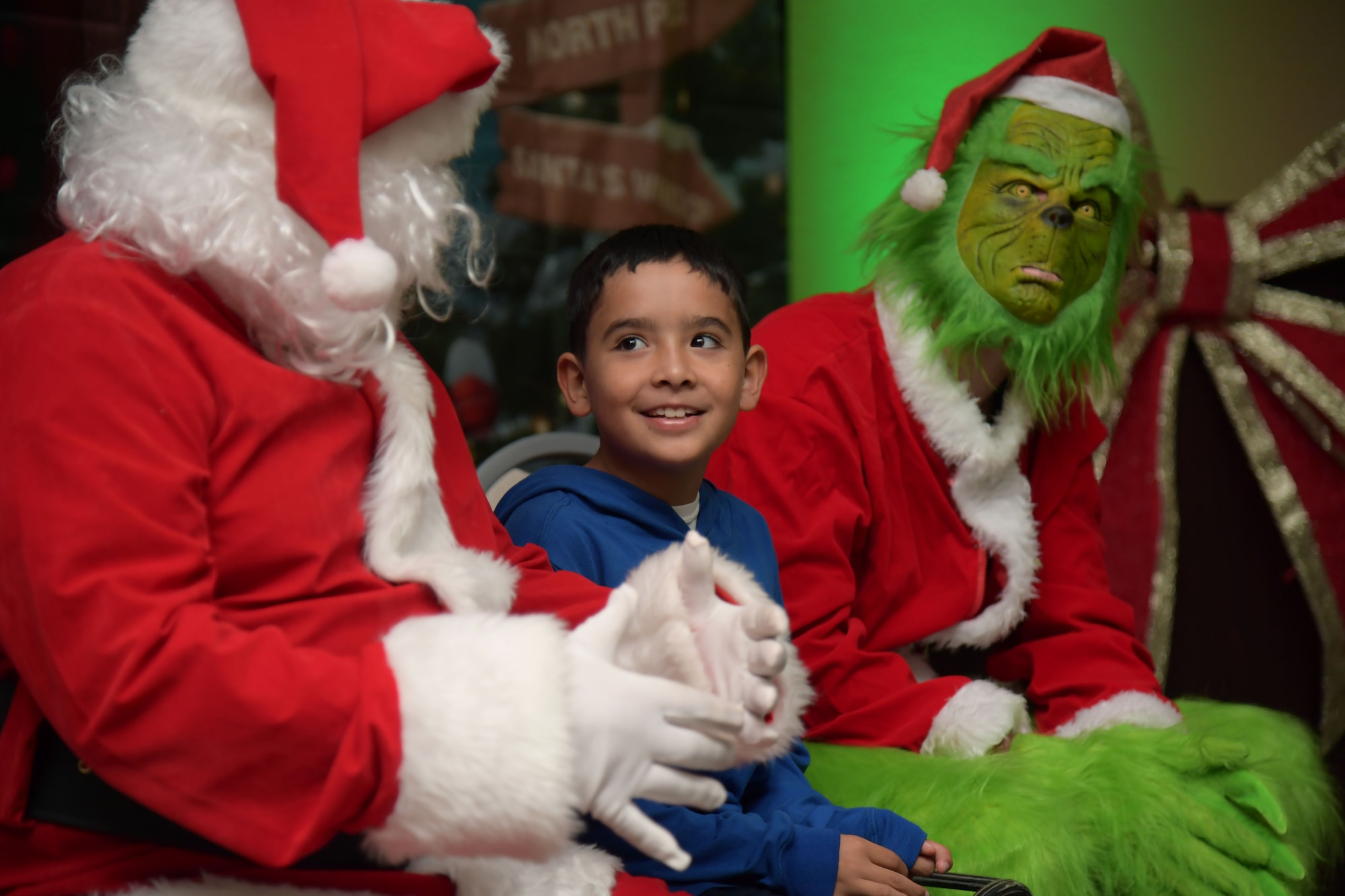 A child sits between Santa Claus and The Grinch.