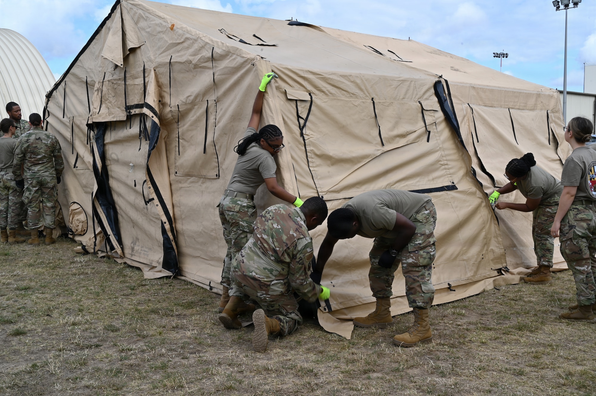 Members of the Maryland Air National Guard assigned to the 175th Force Support Squadron tie down the edges and complete the assembly of a tent as part of their annual training at Royal Air Force Mildenhall, England, July 18, 2025. Military tent facilities are used for a variety of purposes in deployed scenarios, whether it is for a dining hall, an event facility, or even temporary lodging. (U.S. Air National Guard Photo by Staff Sgt. Alexandra Huettner)