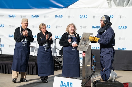 From left, Rear Adm. Casey Moton, Program Executive Officer, Aircraft Carriers, Newport News Shipbuilding President Kari Wilkinson, and ship’s sponsor Pam Bove, applaud NNS welder Andrew Kahler after he welded the initials of Bove onto a metal plate during the keel authentication ceremony for Virginia-class attack submarine Barb (SSN 804) on Tuesday, Dec. 9, 2025 at HII’s Newport News Shipbuilding division. The metal plate will remain affixed to the submarine throughout its life.