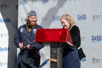 At the weld stand, ship’s sponsor Pam Bove traces her initials on a metal plate during the keel laying ceremony for Virginia-class attack submarine Barb (SSN 804) at HII’s Newport News Shipbuilding division on Tuesday, Dec. 9, 2025. At left is NNS welder Andrew Kahler.