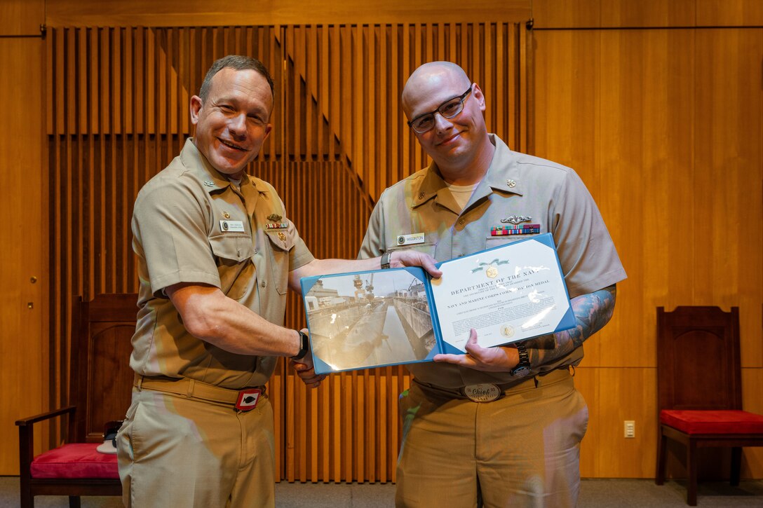 ENS Brett Wiggington, formerly Chief Electronics Technician (Nuclear), receives an award from U.S. Navy Capt. Michael Eberlein during a commissioning ceremony.