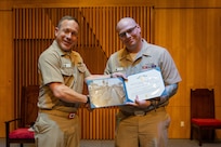ENS Brett Wiggington, formerly Chief Electronics Technician (Nuclear), receives an award from U.S. Navy Capt. Michael Eberlein during a commissioning ceremony.