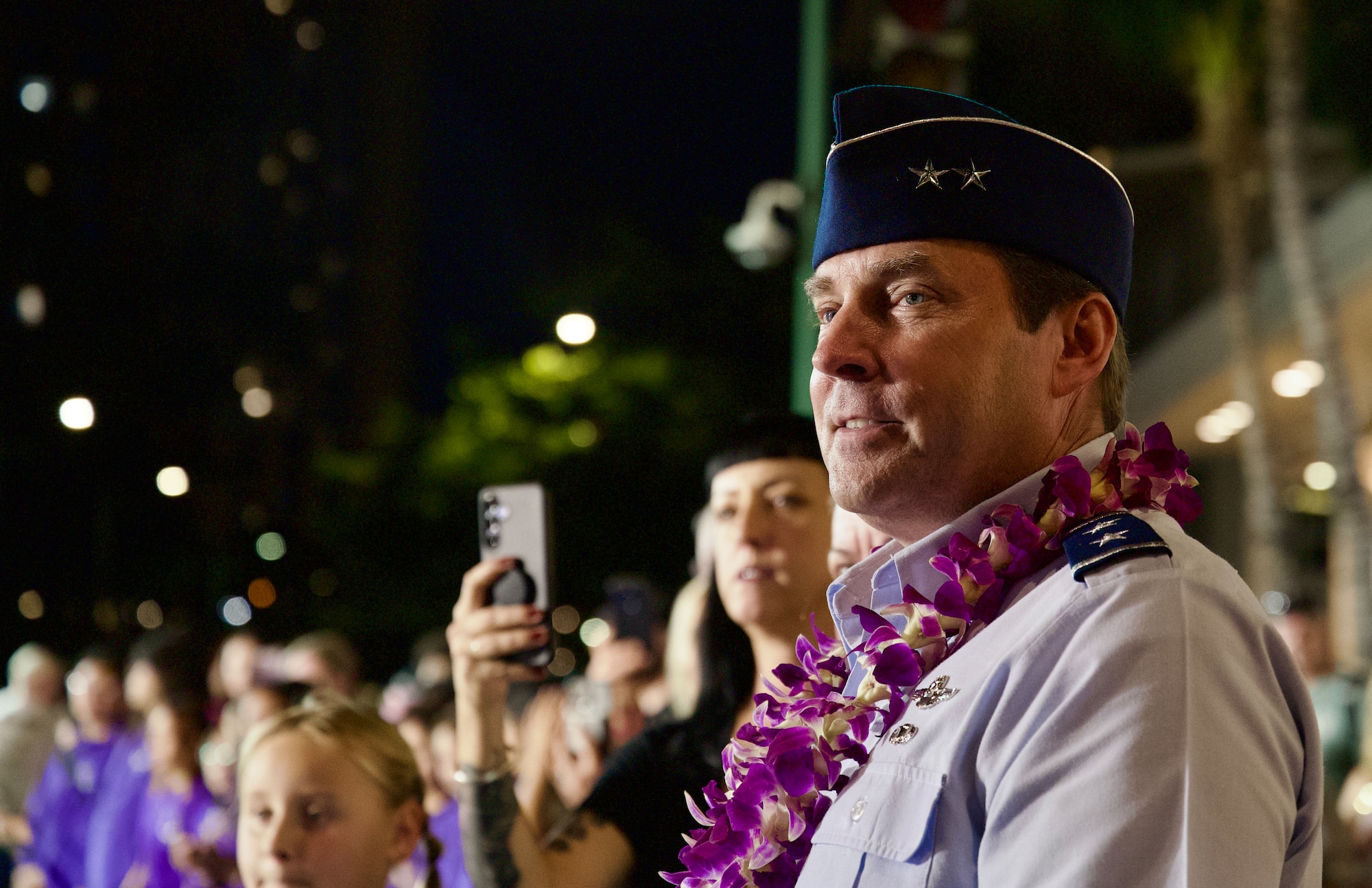 A close up of a senior military officer softly smiling and watching a parade from the side of the road.