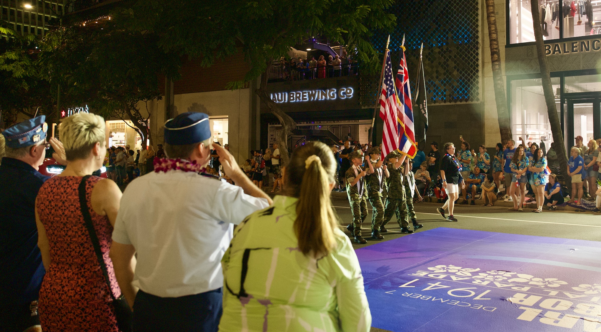 A male senior military officer salutes a formation of color guard personnel marching in a parade holding flags.