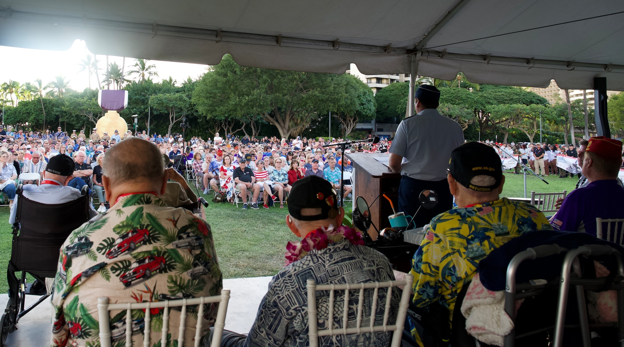 A male senior military officer gives a speech to a crowd of hundreds from a podium on a stage.