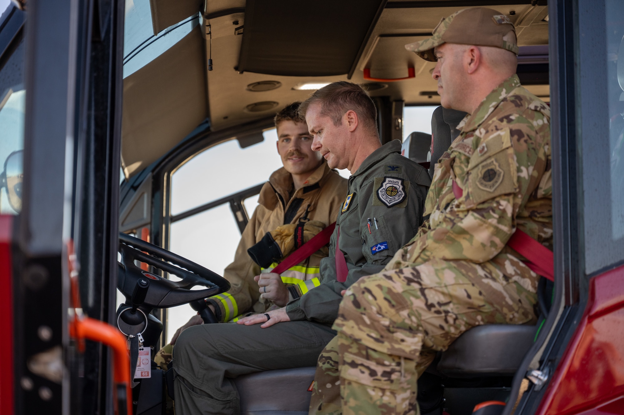 Col. Richard Kind (center), 97th Air Mobility Wing commander, and Col. Adam Rosado (right), 97th Air Mobility Wing deputy commander, are taught how to operate controls on a firetruck by Senior Airman Michael Mikolajczyk (left), 97th Civil Engineer Squadron driver operator, at Altus Air Force Base, Oklahoma, Nov. 4, 2025. The command team used the firetruck’s front-mounted water cannon to extinguish flames on a simulated airplane fire. (U.S. Air Force photo by Airman 1st Class Nathan Langston)