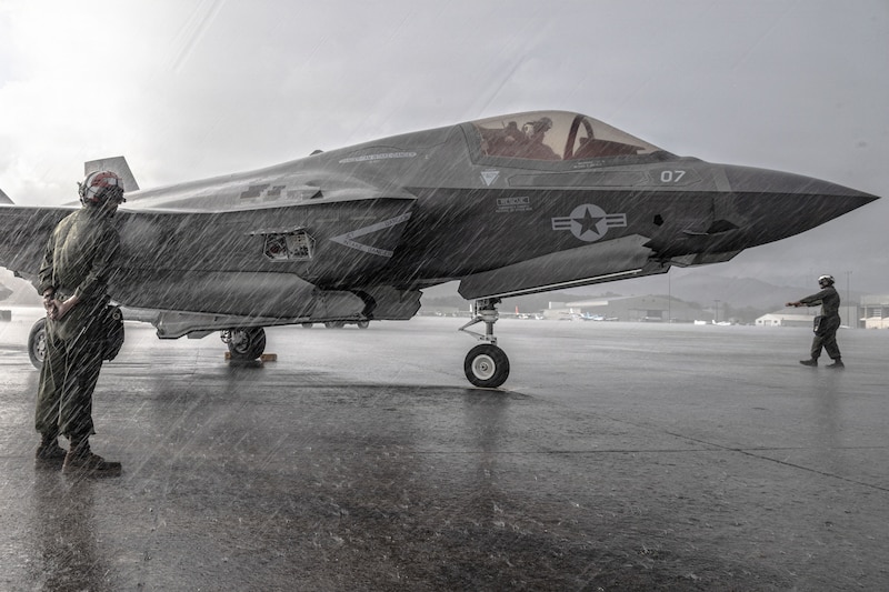 Two Marines stand on a rainy flight line near a parked aircraft.